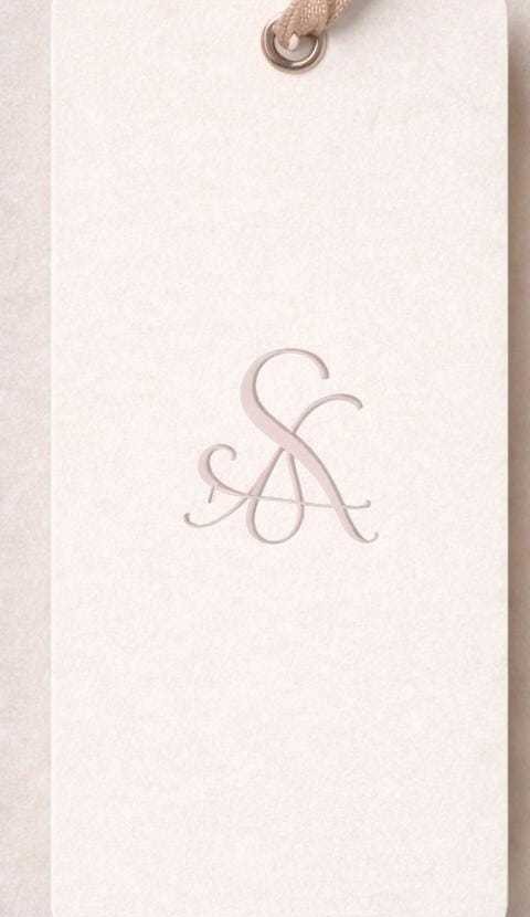 The real Saga hang tag: cream cardstock with the hand-embroidered "S·A" monogram in rose gold, ribbon-tied.